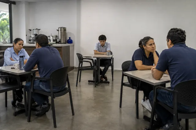 Empleado permanece aislado entre grupos tensos en el comedor del personal.